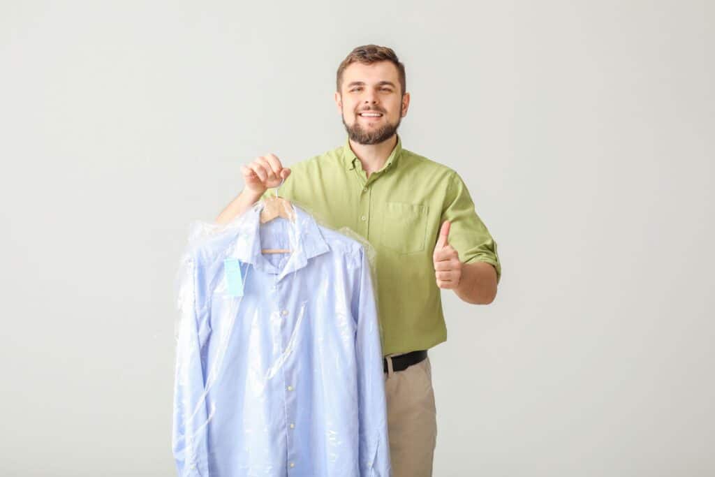 man with thumb up in approval holding dry cleaned shirt